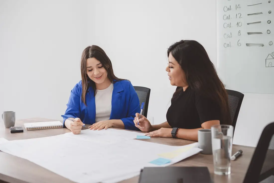 Dos profesionales trabajando juntas sobre un plano en una sala de reuniones